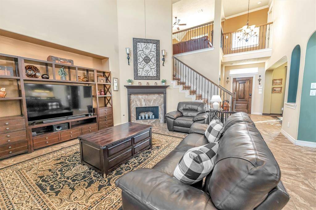 Experience the charm of this spacious living room with its high ceilings and cozy fireplace. Spacious area for seating and an open staircase to a second-floor balcony enhance the inviting, naturally lit space.