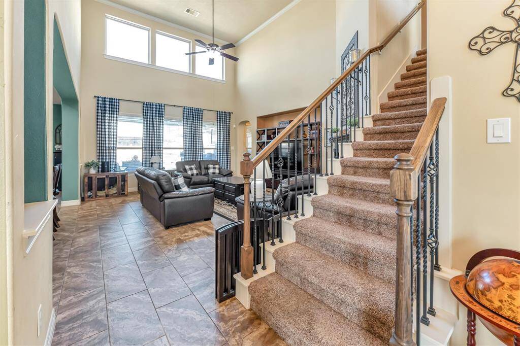 Discover a bright, open living area with high ceilings and large windows. Enjoy the tiled flooring, cozy seating, and a stylish carpeted staircase leading upstairs.