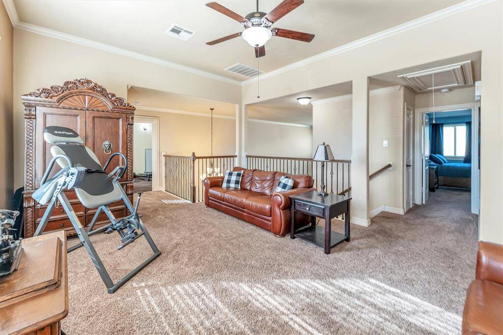 Explore this inviting, carpeted upstairs living area featuring neutral tones, a ceiling fan, and various seating options. Open railing with a view of the floor below. A hallway conveniently leads to one of the three bedrooms.