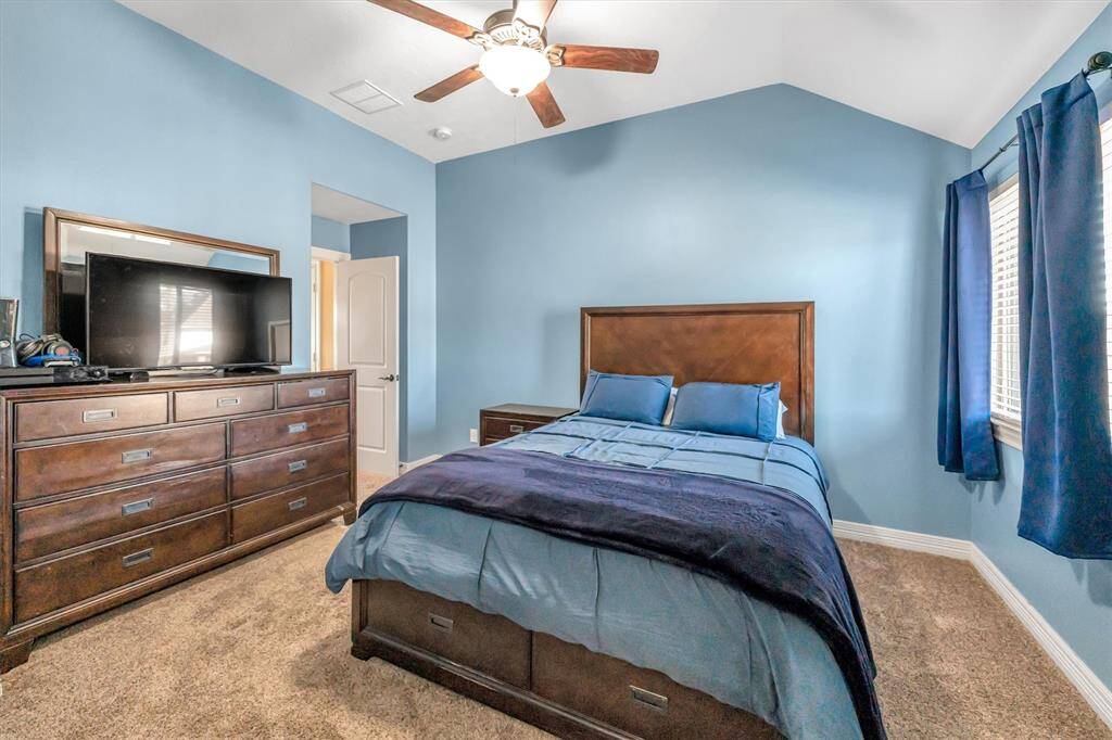 Cozy bedroom with blue walls, featuring a double bed, dark wood furniture, and a ceiling fan. Large windows with  curtains fill the space with inviting natural light.