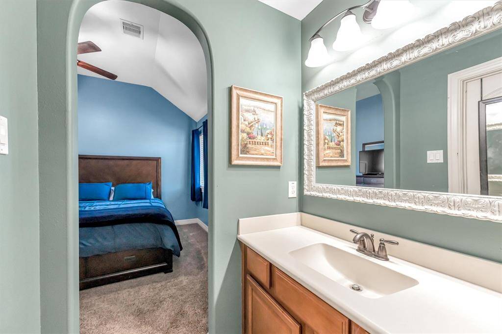 This inviting bedroom features a vaulted ceiling, with an arched entrance to a modern bathroom. The bathroom boasts a single vanity, a large decorative mirror, and contemporary lighting.