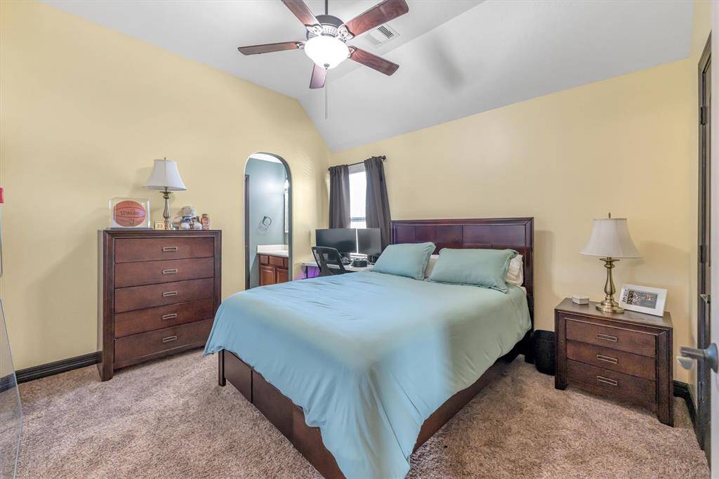 Inviting bedroom features soft yellow walls, a vaulted ceiling with a fan, and plush carpeting. An arched doorway adds charm and connects to the jack-n-jill bath.