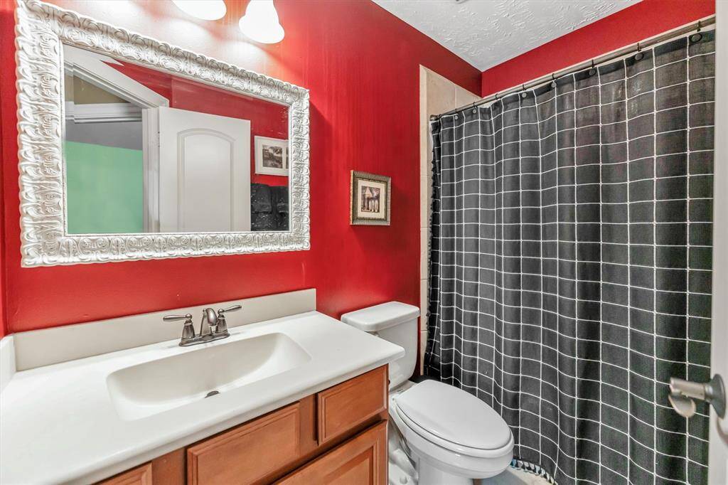 Stylish bathroom features bold red walls, a large ornate mirror, and a sleek white vanity with wood cabinetry. It includes a shower/bath combo.