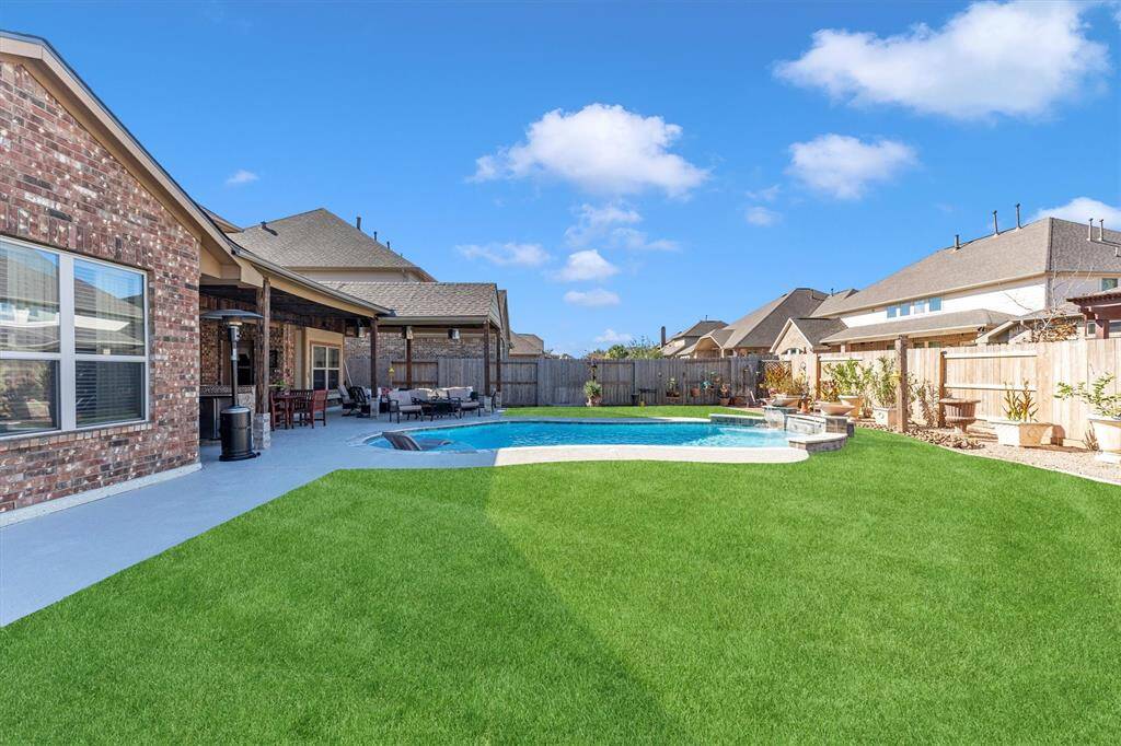 This backyard offers a spacious lawn featuring artificial grass, a stunning pool, and a covered patio ideal for entertaining.