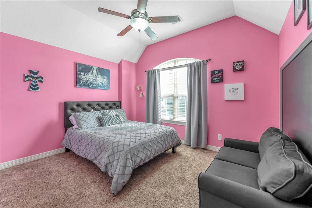 Inviting bedroom boasts vibrant pink walls, a vaulted ceiling with a modern fan, and a large arched window for ample natural light complete the welcoming space.
