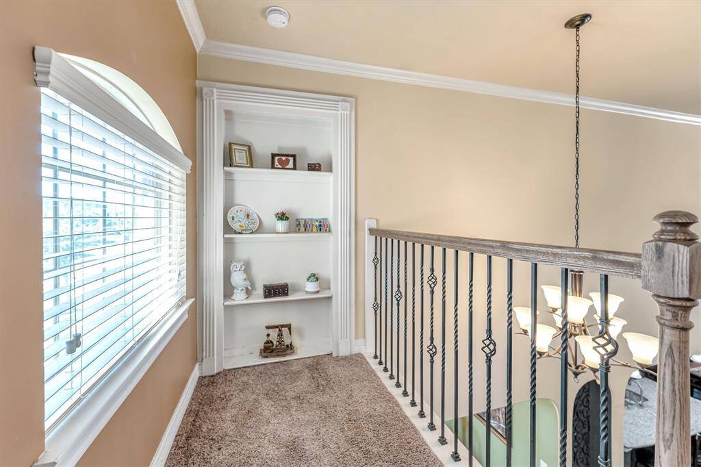 Cozy landing with a built-in bookshelf, plush carpet, elegant light fixture, and decorative railing. Ideal for a reading nook or display space.