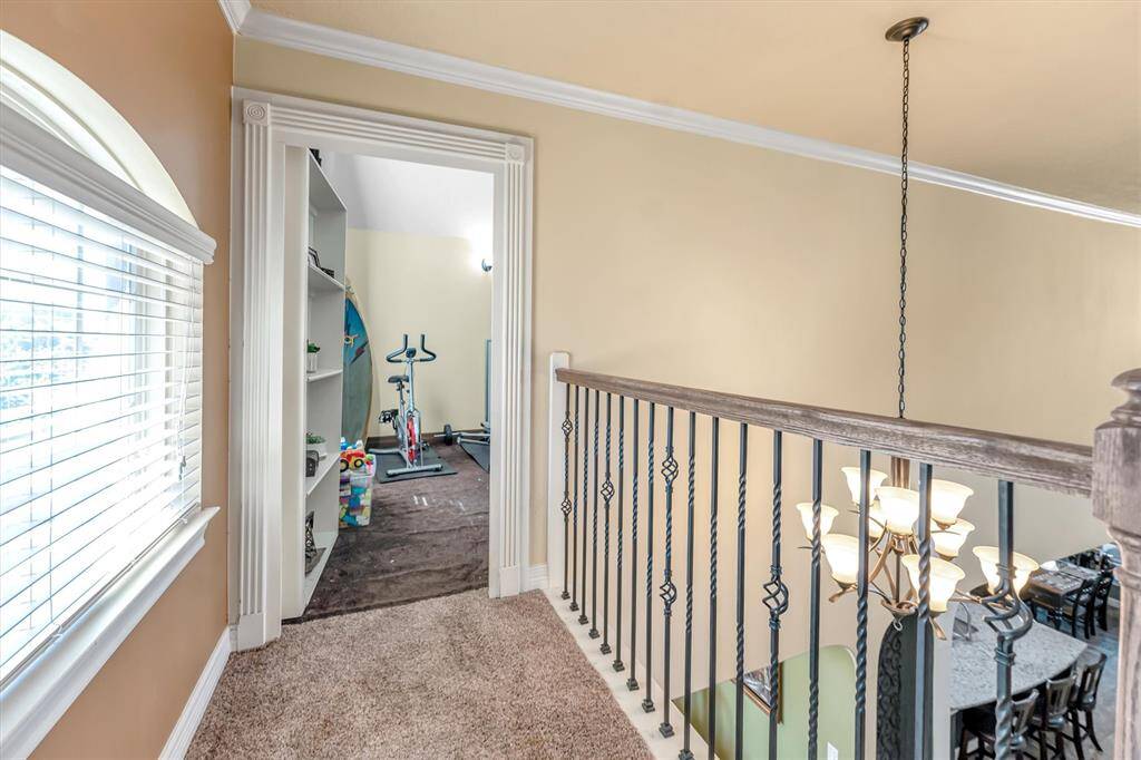Experience the charm of this cozy upstairs landing with plush carpeting and stylish iron railings. It seamlessly connects to a bright, versatile hidden room perfect for a home gym, featuring an exercise bike and ample shelving. The room is wired for sound to be used as a media room.