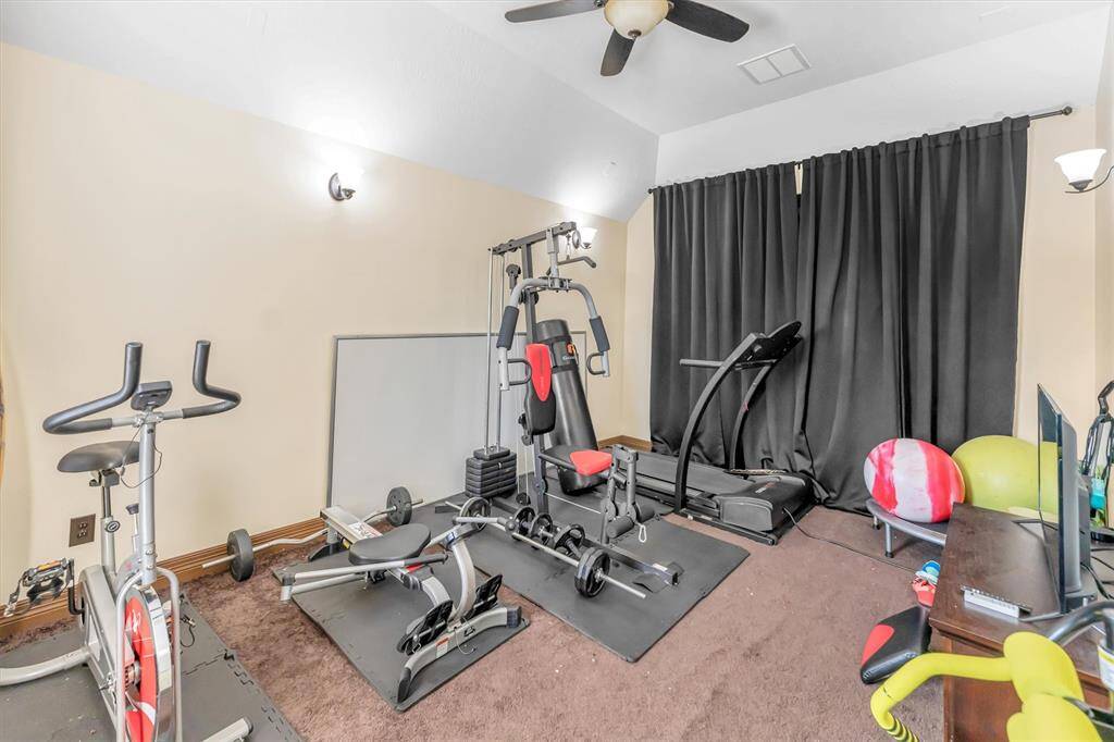 This cozy home gym/media room with a ceiling fan and dark curtains for privacy, it's perfect for personal workouts or movie nights.