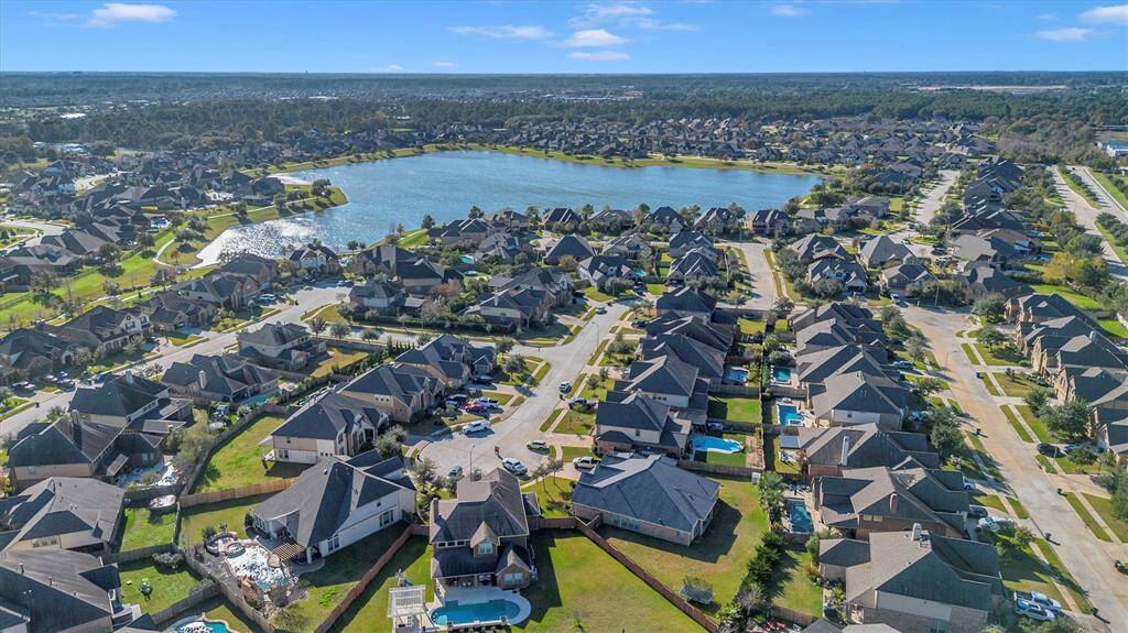 Aerial view of a charming suburban neighborhood with pristine homes, some with pools, nestled in lush greenery near a scenic lake for a peaceful, picturesque setting.