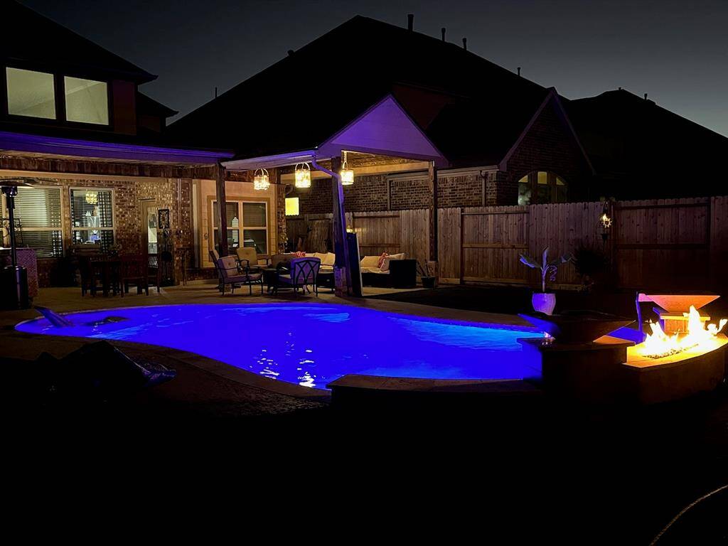 Night view of the backyard featuring the poolside fireplace.