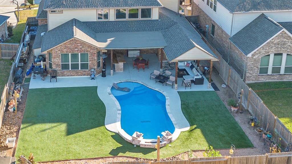 Experience ultimate relaxation and entertainment in this spacious backyard, featuring a stylish curvy pool, a cozy covered seating area, and a lush, artifical  lawn.