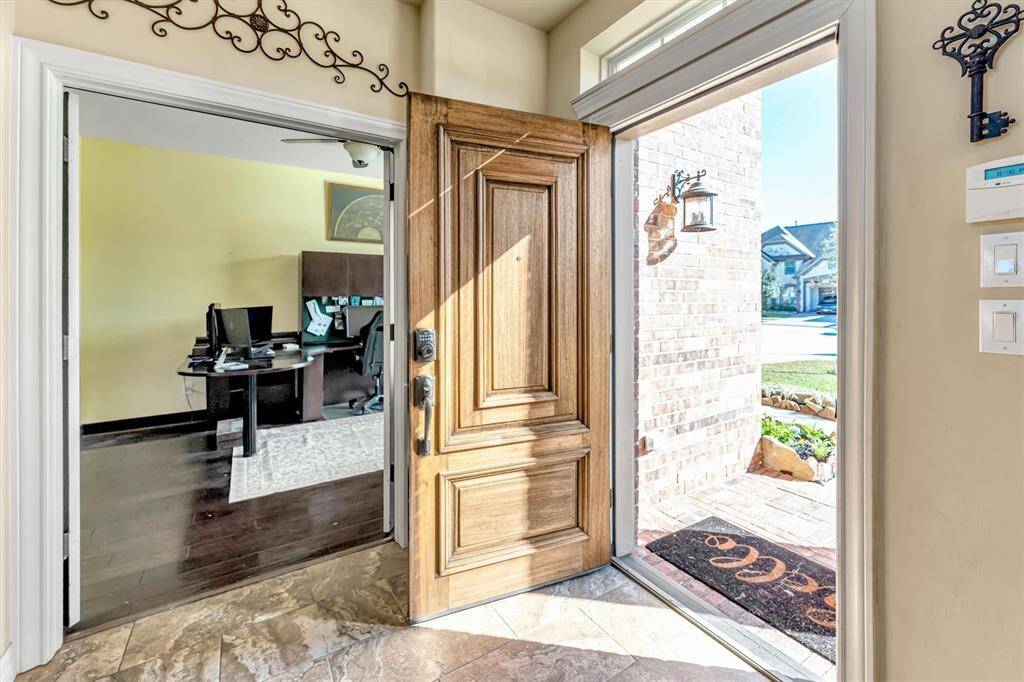 Bright entryway with a wooden door opens to a home office featuring sleek dark flooring and a well-kept neighborhood view.