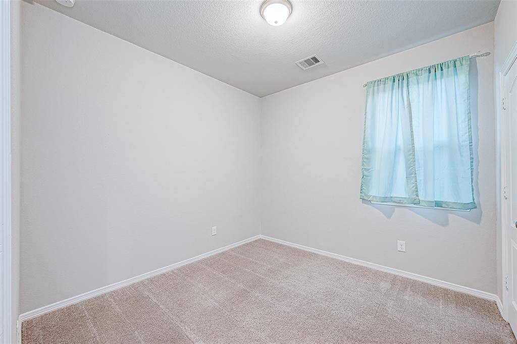 A cozy room with light beige walls and carpet, featuring a single window with light blue curtains and a ceiling light fixture. Perfect for a bedroom or home office