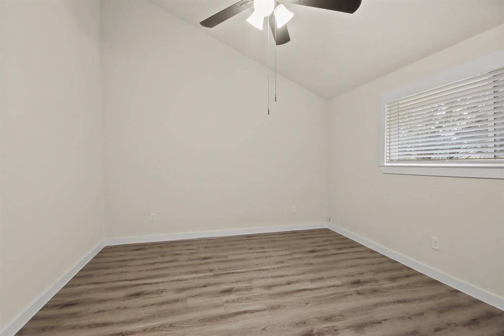 This room features a modern, clean look with fresh  walls and wood-style flooring. It has a high ceiling with a ceiling fan and a window with blinds, offering plenty of natural light. Perfect for a bedroom or office space.
