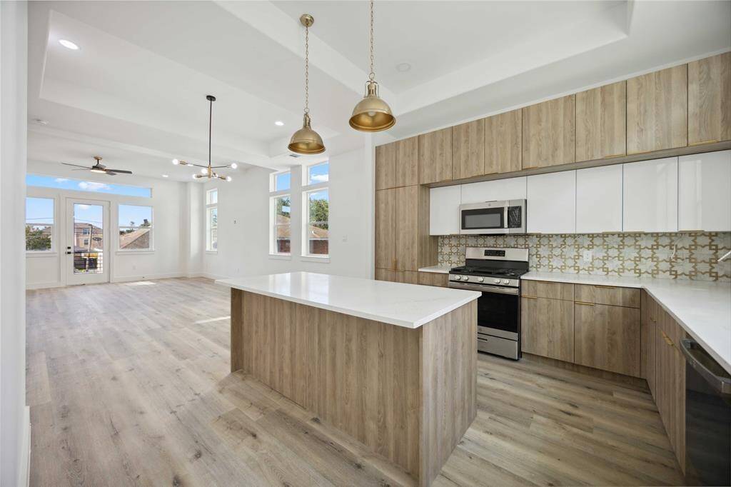 Spacious, modern kitchen featuring light cabinetry, white countertops, and stainless steel appliances. Enjoy an oversized island, pendant lighting, and ample natural light streaming in from the large windows. The open floor plan allows for an easy flow into the adjacent living area!