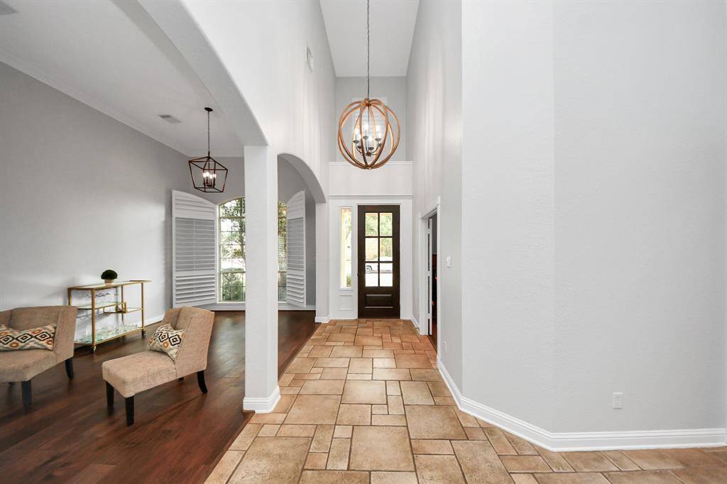 Entryway features high ceiling with a modern chandelier, tiled flooring leading to a wooden front door, and an open archway to use as a flex space.