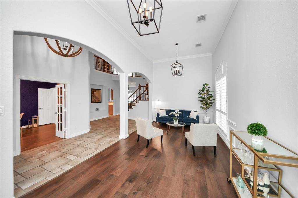 This inviting home features a bright, open flex space area with high ceilings and modern light fixtures. The space combines elegant wood and tile flooring. A staircase leads to the upper level, adding a touch of grandeur.