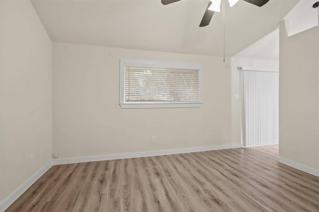 This room features light walls and wood flooring, a ceiling fan, a window with blinds, and sliding glass doors leading outside, creating a bright and airy space.
