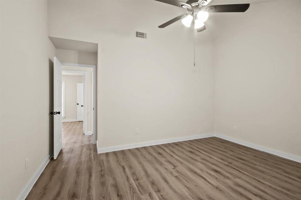 This room features a clean, neutral palette with light walls and wood-style flooring. It has a ceiling fan and natural light from a doorway, creating a bright, airy space perfect for a bedroom or office.
