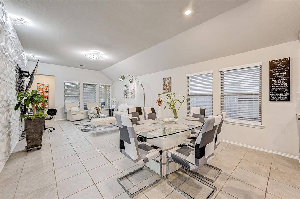 This photo showcases a modern, open-plan living and dining area with a sleek, contemporary design. It features a glass dining table with stylish chairs, tiled flooring, and a distinctive textured wall. The space is well-lit with large windows and decorative ceiling lights, creating a bright and welcoming atmosphere.