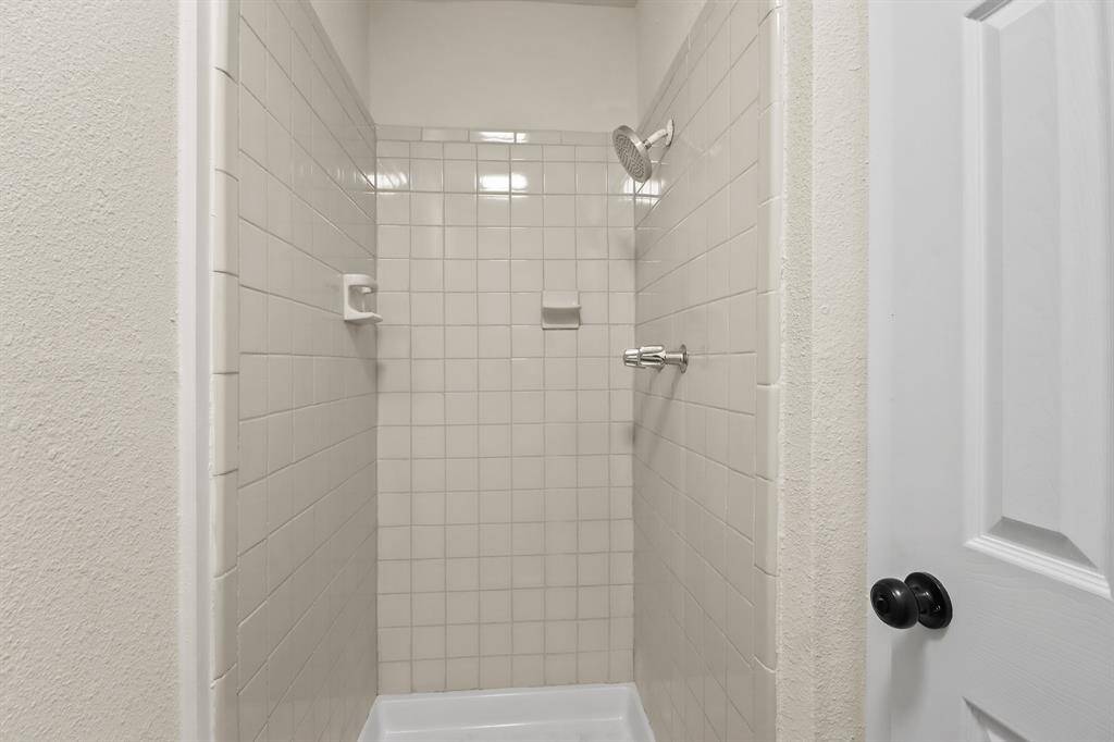 This photo features a compact, tiled shower with a simple design. It includes a showerhead and small built-in shelves for convenience.