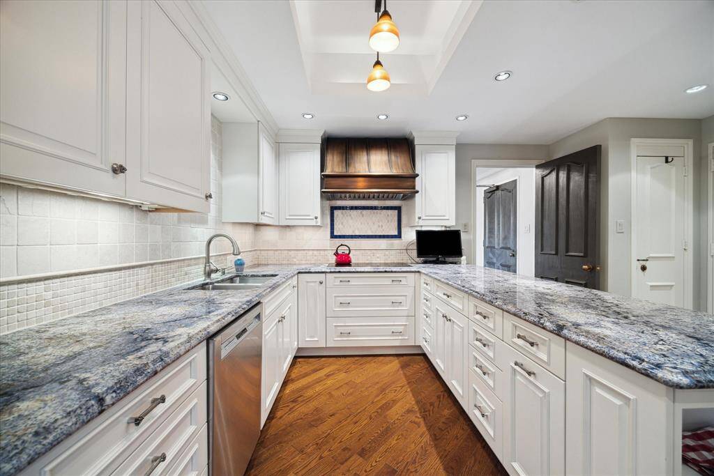 Partial view of kitchen which offers abundant storage plus  Wolf microwave, convection oven and 5-burner electric cook top. New Bosch dishwasher. Copper vent hood and stone backsplash.  Beautiful granite counters.