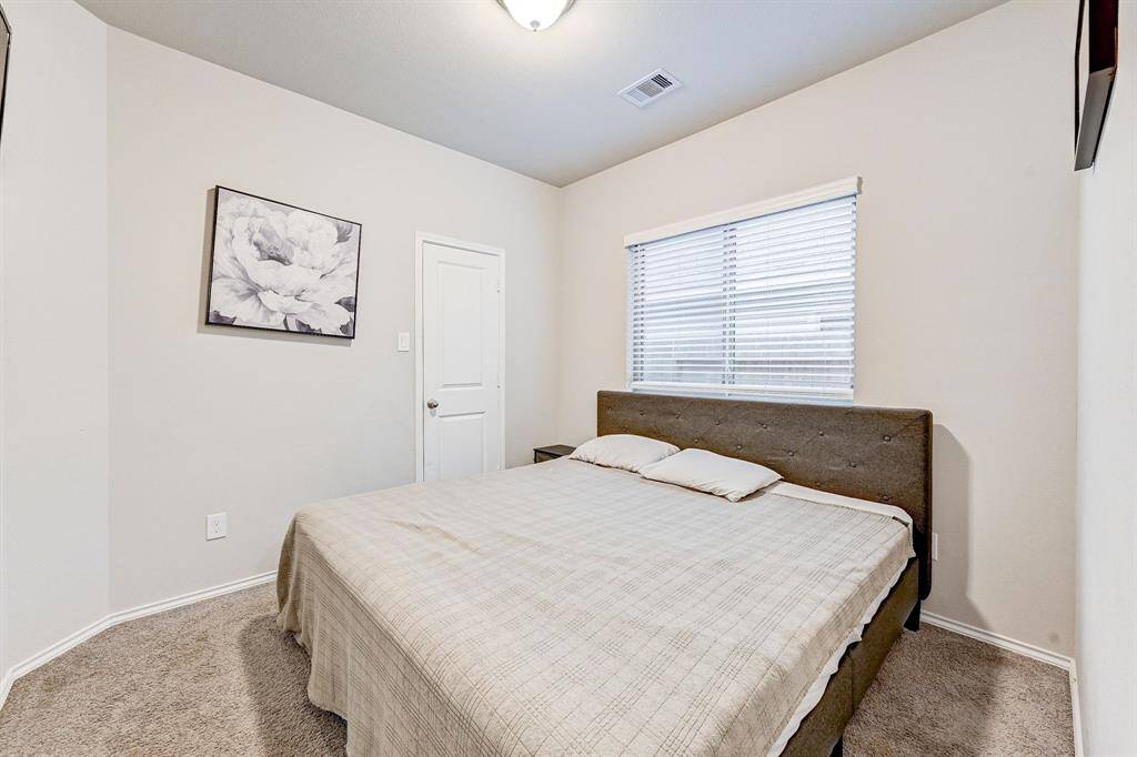 This cozy bedroom features neutral walls, plush carpeting, and a window with blinds for natural light. The space includes a comfortable bed and a simple door leading to additional storage or a closet. Ideal for a restful retreat.