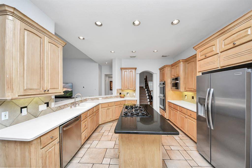 Spacious kitchen with natural wood cabinets, modern stainless steel appliances, newly installed double oven & microwave with a central island featuring a gas cooktop. The layout offers ample counter space and a bright, open feel, perfect for cooking and entertaining.