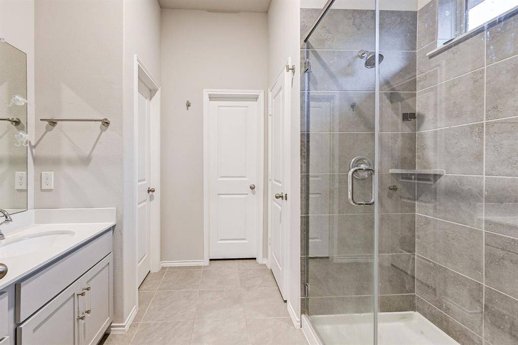 This bathroom features a modern glass-enclosed shower with sleek gray tiles, a wide vanity with a white countertop, and ample mirror space. The neutral color palette and clean lines create a bright, contemporary feel.