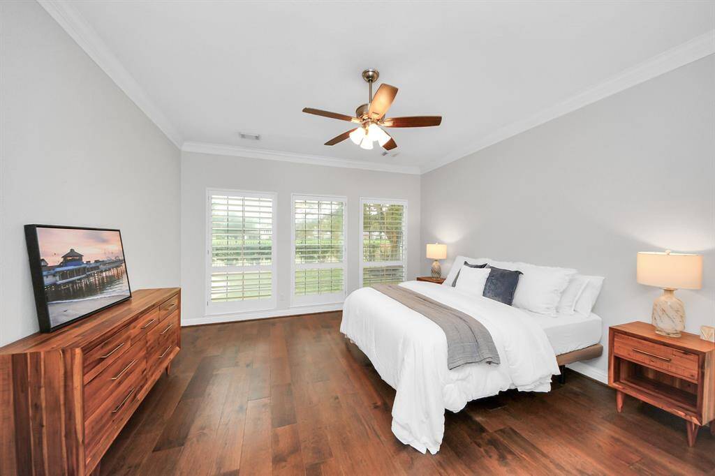 Spacious primary bedroom with hardwood floors, featuring a large window with plantation shutters for natural light.