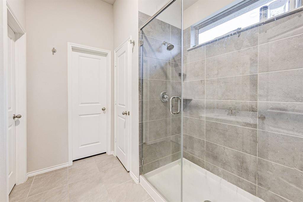 This bathroom features a spacious walk-in glass shower with modern gray tile, complemented by light tile flooring. It includes two white doors, providing a clean and bright ambiance.