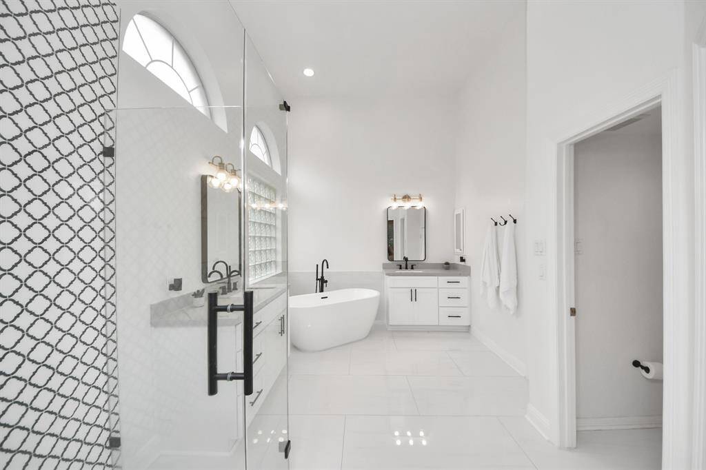 This bathroom features a modern design with a standalone tub, dual vanities, and a large glass-enclosed shower. The space is bright and airy, thanks to high ceilings and ample natural light.