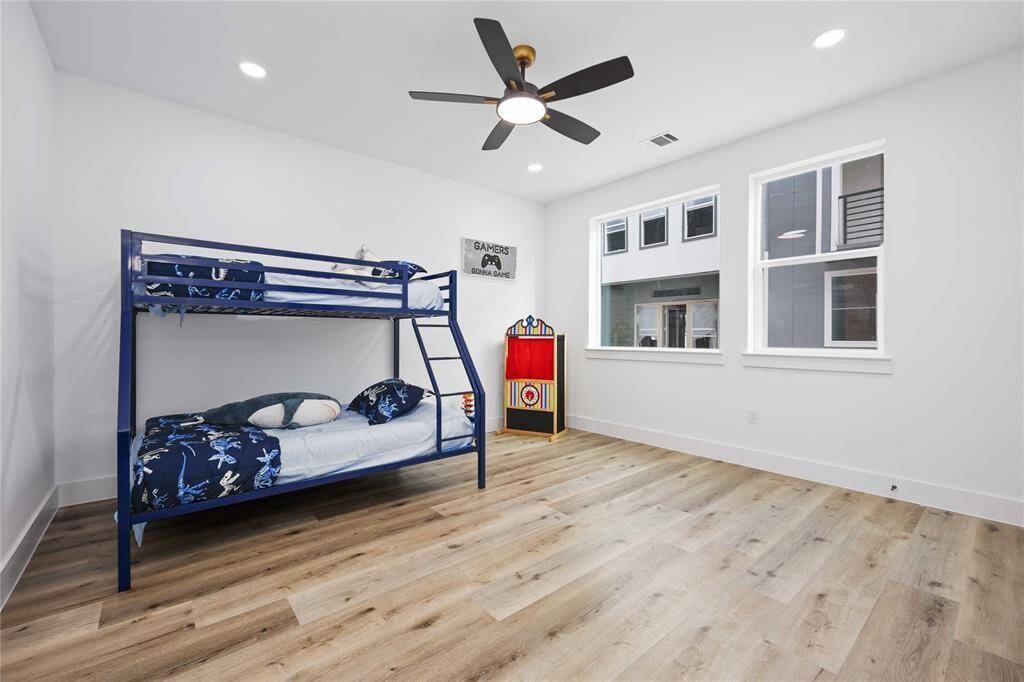 Secondary bedroom on second floor features high ceiling with modern ceiling fan and stylish upgraded flooring. It includes a walk-in closet and ample natural light from oversized windows, promising a cozy and inviting space for personalization.