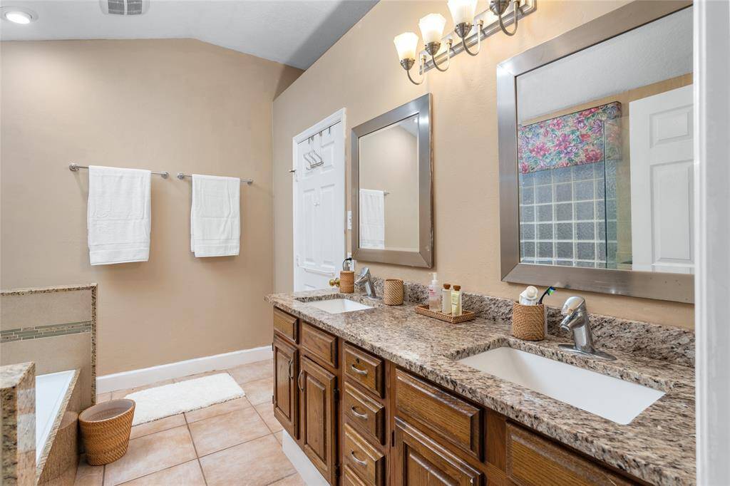 The primary bath features double sinks with separate framed mirrors, offering plenty of space for both his and her items. With its spacious layout, it ensures a comfortable and organized experience, making daily routines feel more efficient and enjoyable.