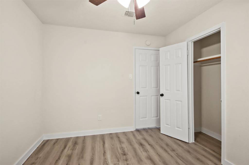 This room features neutral walls, wood-look flooring, a ceiling fan, and a small closet with a white door, creating a simple and clean space.