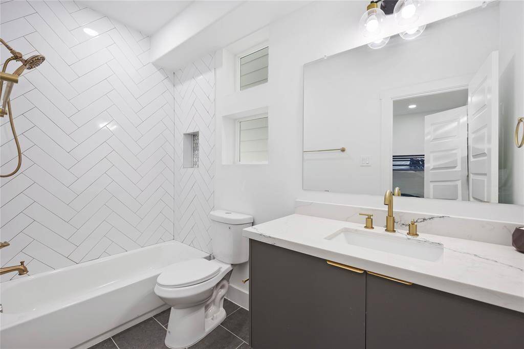 Secondary bathroom on second floor features sleek cabinetry, white countertops, gold-tone fixtures. A combination tub and shower with tile surround and built-in niche for toiletries complete the space.