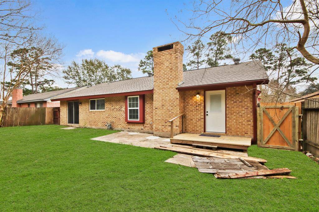 This photo shows a cozy brick home with a spacious backyard. It features a small wooden deck, a chimney, and a fenced area, perfect for outdoor activities.