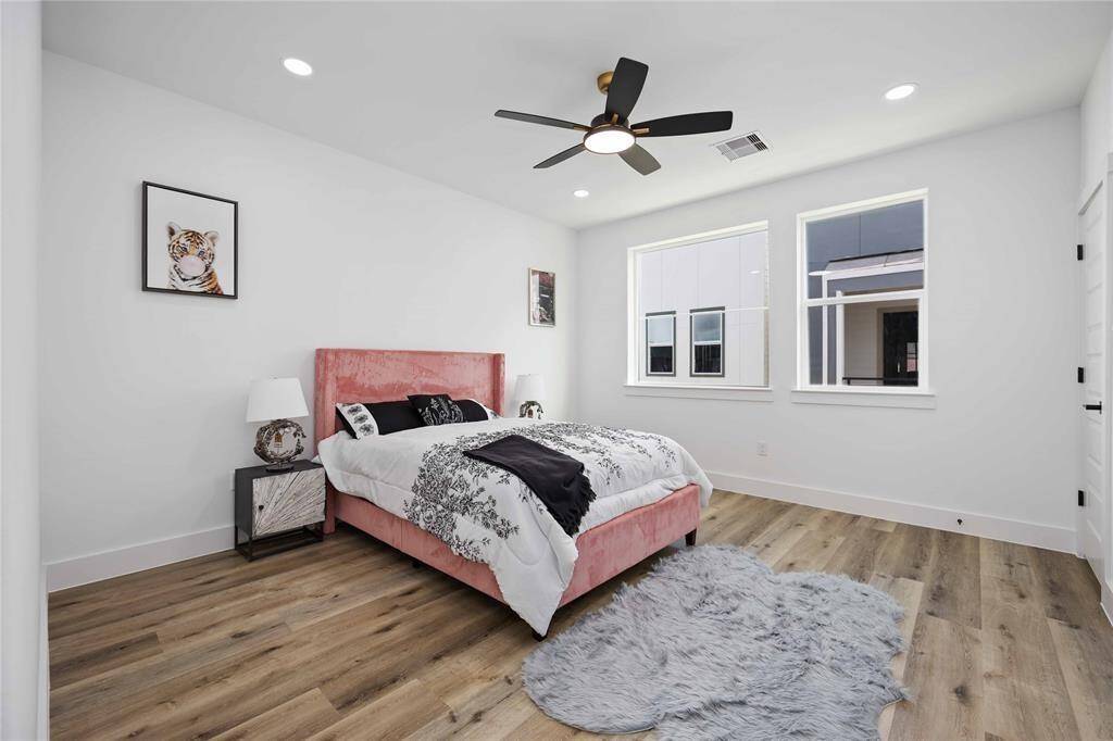 Secondary bedroom on third floor features high ceiling with modern ceiling fan and stylish upgraded flooring. It includes a walk-in closet and ample natural light from oversized windows, promising a cozy and inviting space for personalization.