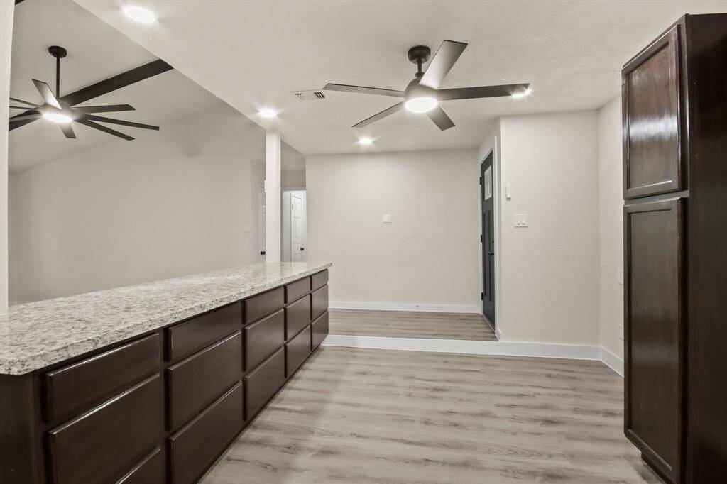This modern space features a spacious room with light wood flooring, a large granite countertop with ample storage, and contemporary ceiling fans, creating a bright and functional area ideal for a kitchen or living space.