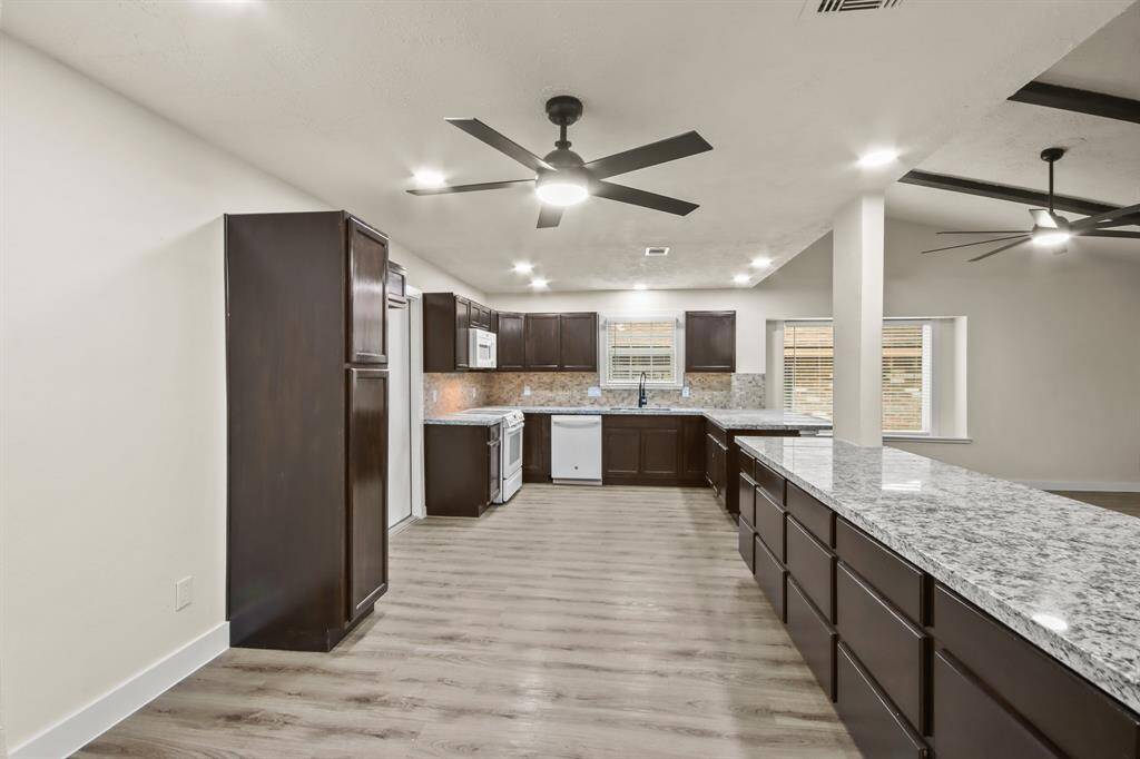 This photo showcases a spacious, modern kitchen with dark wood cabinets, granite countertops, and stainless steel appliances. The room features wood flooring, recessed lighting, and ceiling fans, providing a bright and open feel.