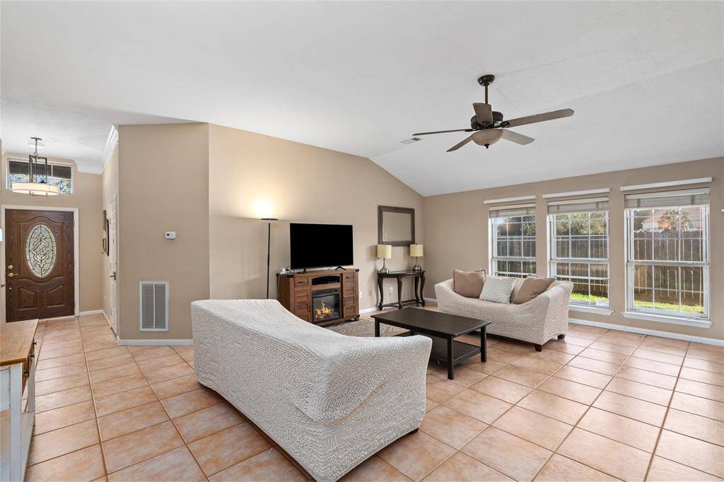 The living room boasts a striking wall of windows, filling the space with abundant natural light and offering beautiful views of the outdoors. A charming fireplace creates a cozy focal point, perfect for gathering and enjoying peaceful moments.