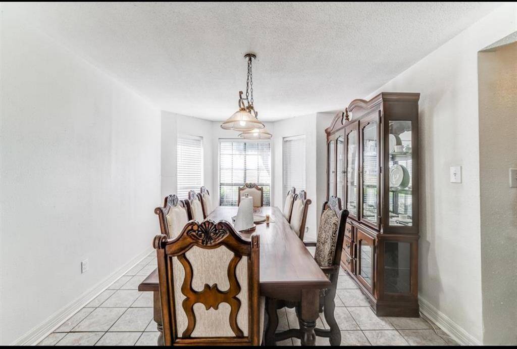 This photo shows a bright dining room with a large wooden table, elegant chairs, and a matching china cabinet. The space is well-lit by natural light from multiple windows, creating a welcoming atmosphere.