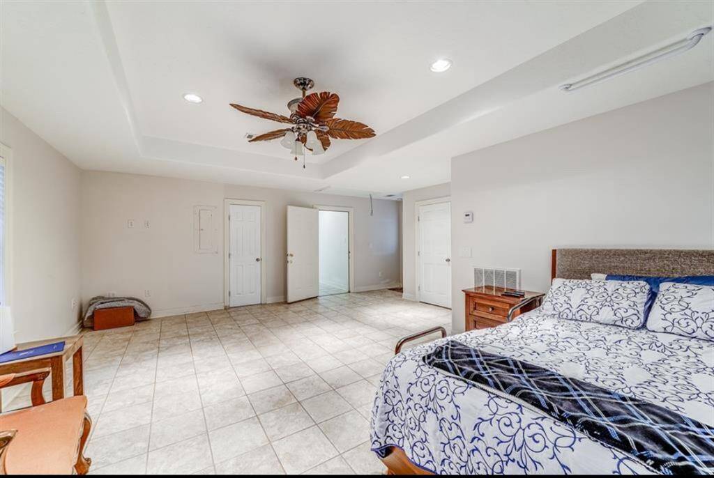 Spacious bedroom with tiled flooring and a ceiling fan. It features neutral walls, ample natural light, and dual closets for extra storage.