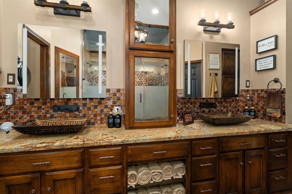 This luxurious primary bathroom features a spa-like atmosphere with a focus on functionality and style. The vanity boasts dual sinks with ample counter space, perfect for getting ready in the morning or sharing the space with a partner. The bathroom is adorned with granite counters, decorative mirrors and stylish lighting fixtures, creating a warm and inviting ambiance.