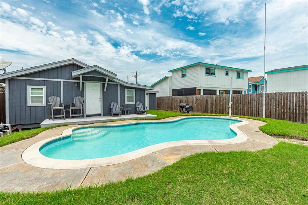 This image showcases the back of the home with a porch and an inviting in-ground swimming pool in a well-maintained backyard, enclosed by a privacy fence. Perfect spot for entertaining