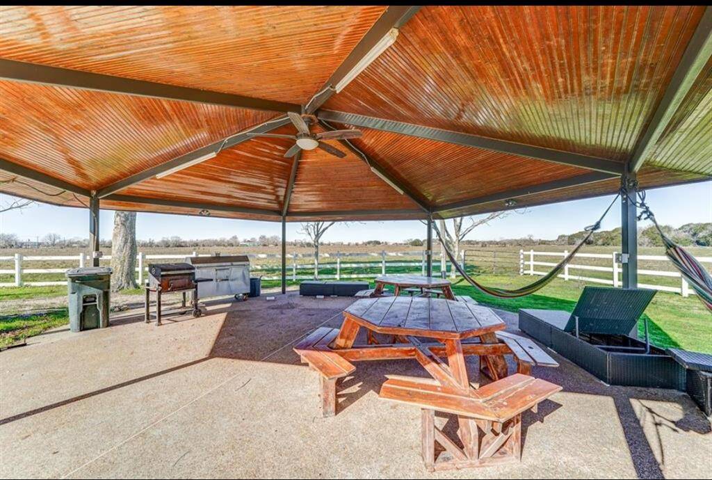 This outdoor space features a spacious gazebo with a ceiling fan, perfect for gatherings. It includes a picnic table, BBQ grill, and hammocks, all overlooking a serene fenced landscape. Ideal for relaxation and entertaining.