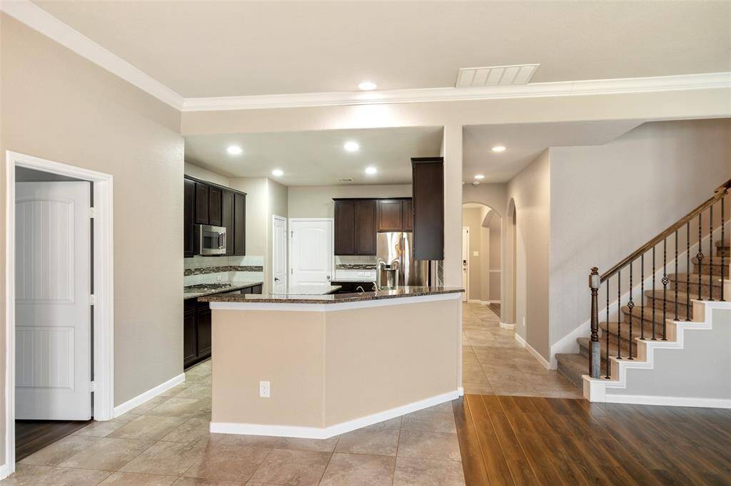 Another view back to kitchen and foyer showing stairway to second floor with wrought iron ballisters. Bar seating available for extra seating