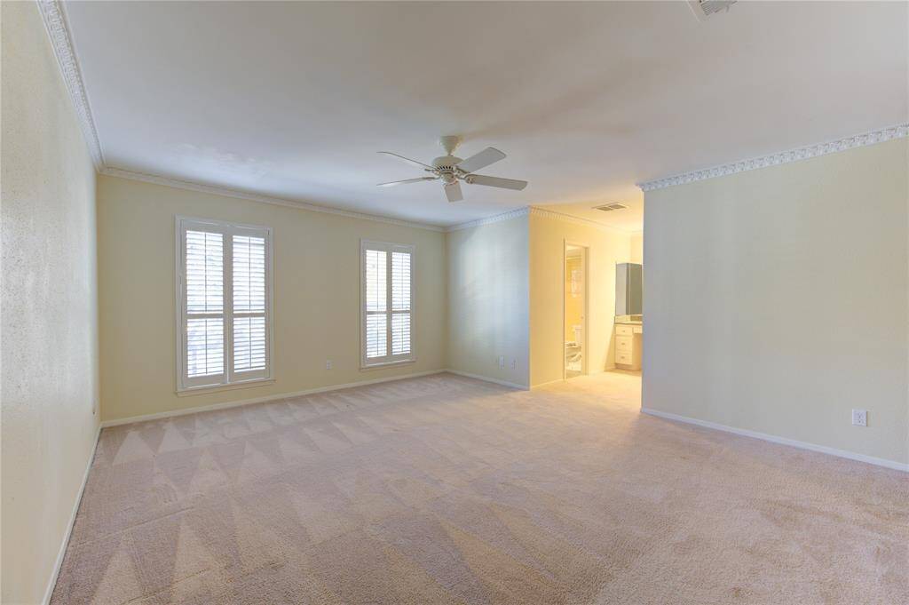 This spacious second bedroom features carpeted flooring, and large windows with shutters, offering plenty of natural light. A ceiling fan adds comfort to the space.