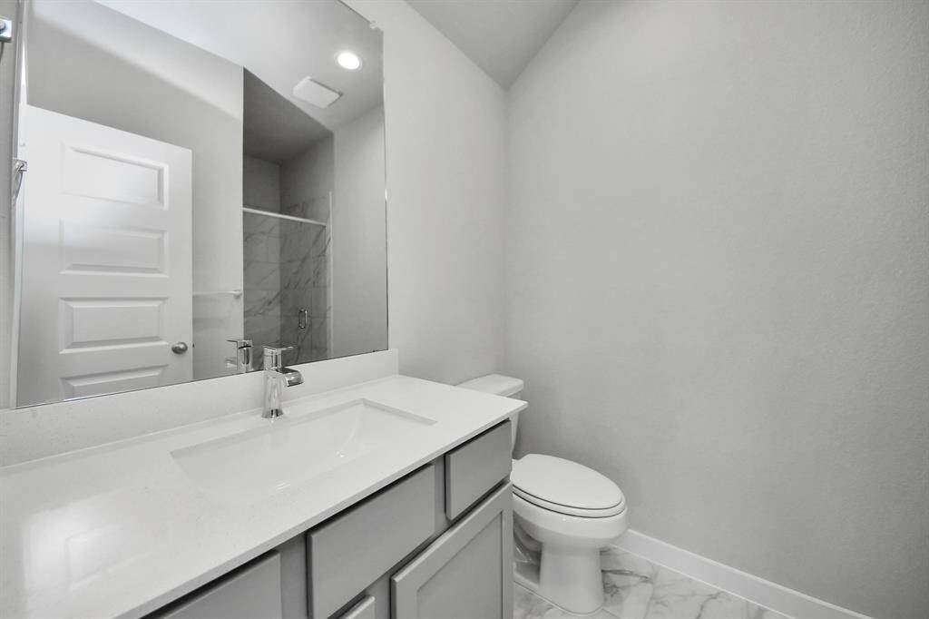 Guest suite bathroom, where tile flooring complements a walk-in shower with tile surround. Wood cabinets completed with a beautiful light countertop, enhances the space for a truly inviting ambiance.