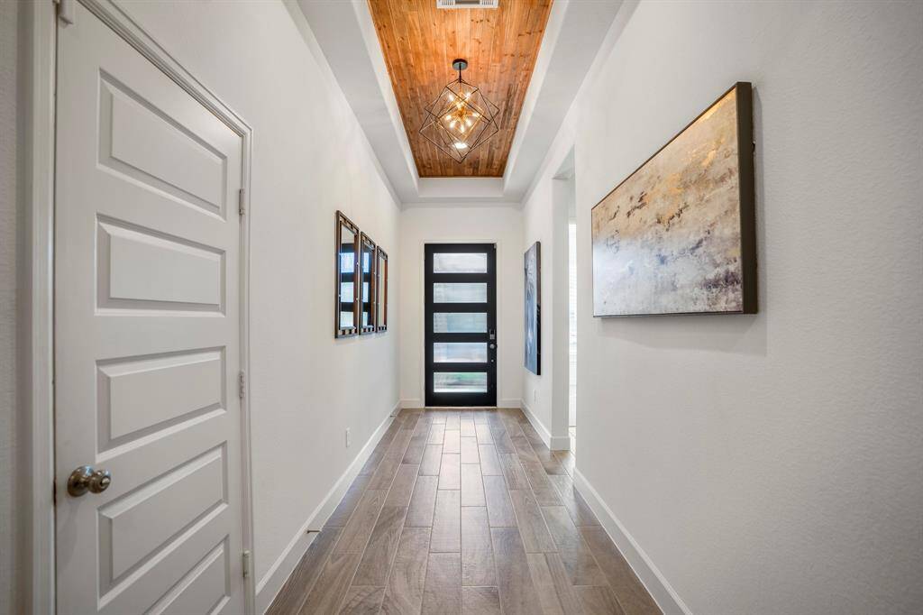 This entryway is a warm and elegant introduction to the home, blending functionality with sophisticated design elements. Tray ceilings with wood paneling and recessed lighting create depth and add character, guiding the eye through the hallway.